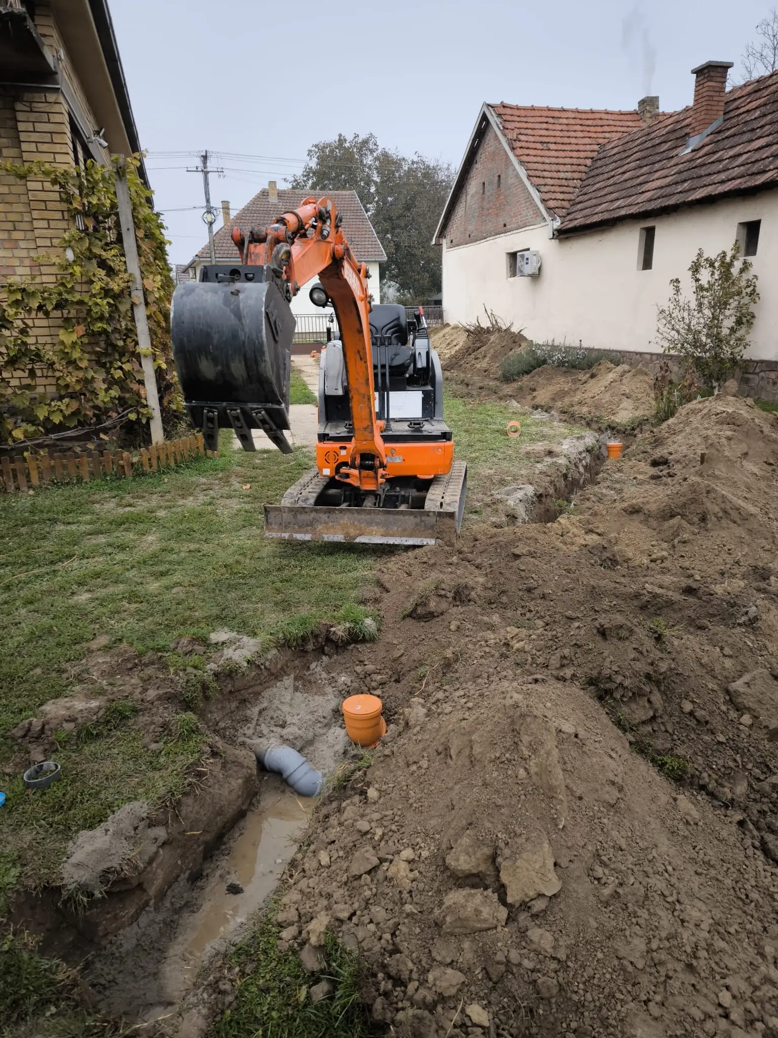 Mini bager kopa kanal za kanalizaciju u uskom prolazu između dve kuće